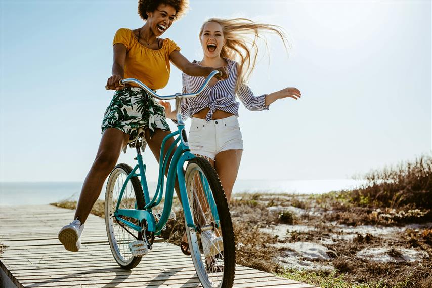 Two girls playing with a bicycle on the boardwalk on a seaside holiday.